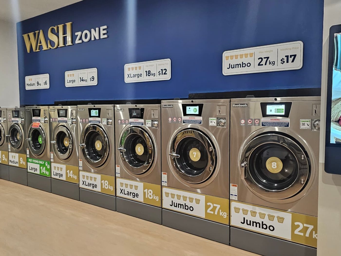 The wall of commercial washing machines at LuxeSpin with size and price signage